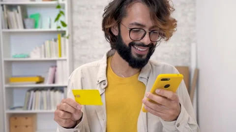 Happy man shopping online using mobile cell phone and credit bank card sitting Stock-Footage 228313007