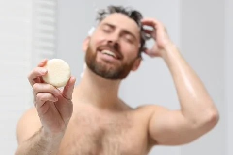 Happy man showing solid shampoo bar in bathroom, selective focus 스톡 사진