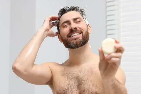 Happy man showing solid shampoo bar in bathroom Stock Photos