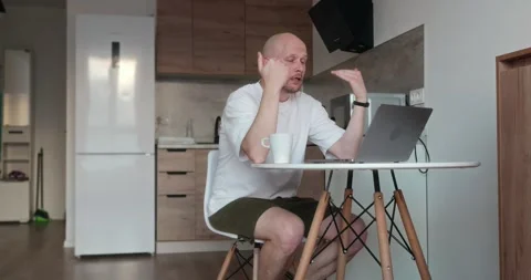 A happy man sits at a table and communicates via video call using his laptop Stock Footage 302901403