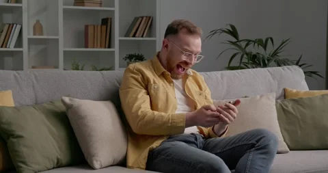 Happy man sitting on cozy sofa in living-room, using modern smartphone. Stock Footage 249465821