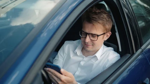 Happy man sitting inside car using a smart phone voice recognition function on Stock Footage 90720867