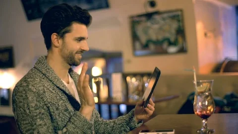 Happy man sitting in a pub and having a videocall on tablet Stock Footage 70126899