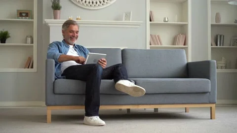 Happy man sitting on sofa, using digital tablet and communicating through video Stock Footage 139751782