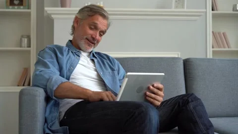 Happy man sitting on sofa, using digital tablet and communicating through video Stock Footage 139751929