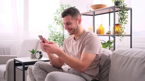 Happy man sitting on sofa using smartphone Stock Footage 171544038