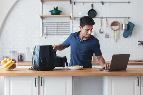 Happy man standing at kitchen table and cooking toast bread by Air Frye machine Stock Photos