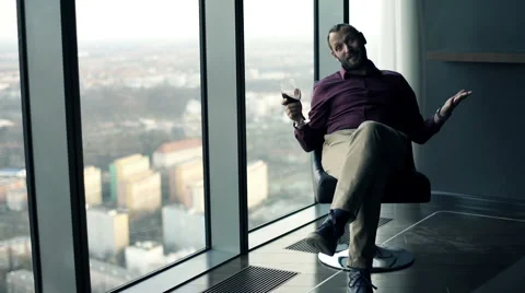 Happy man talking to camera and raising toasty sitting on armchair close to the 動画素材 66768382