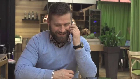 Happy man talking by smartphone, in pub, cafe, indoor, steadicam shot Vídeos de archivo 73069048