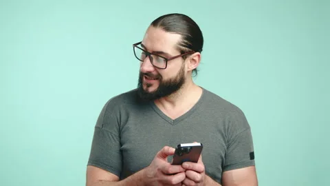 Happy Man Texting on Smartphone with a Big Smile on a Teal Background Stock Footage 268586809