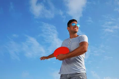 Happy man throwing flying disk against blue sky on sunny day, low angle view Stock Photos