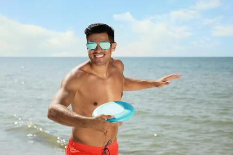 Happy man throwing flying disk at beach on sunny day Stock Photos