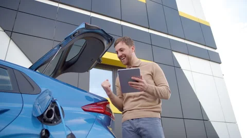 Happy man typing on tablet device while waiting till his electric car charge Stock-Footage 247454794