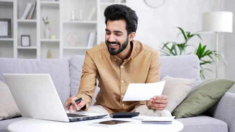 Happy man uses application for spending bills using laptop computer while sit Stock Footage 252214966