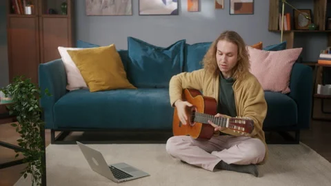 Happy man using laptop computer, playing acoustic guitar sitting on floor Stock Footage 156008383