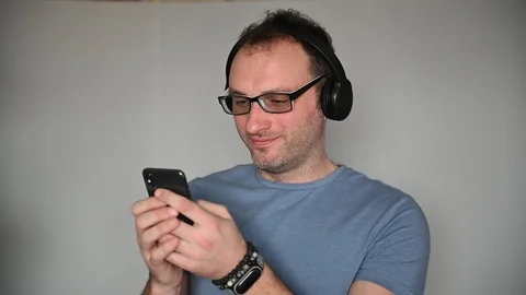 Happy man using mobile phone while listening music on headphones Stock Footage 127210043