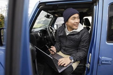 Happy man using smart phone and laptop on road trip in blue jeep Foto stock