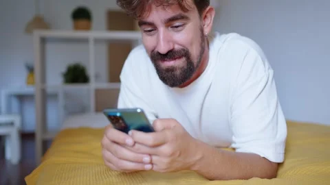 Happy man using smartphone lying on bed at home Stock Footage 316923445