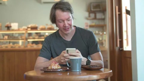 Happy man using smartphone in modern bakery cafe with coffee and raspberry Stock Footage 336320315