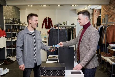 Happy man is using a smartphone to pay by NFC for purchases in a clothing sto Stock Photos