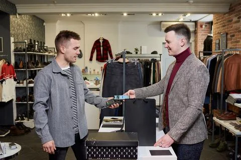 Happy man is using a smartphone to pay by NFC for purchases in a clothing sto Stock Photos