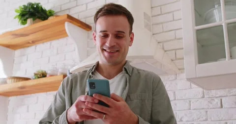 Happy man using smartphone to type SMS text in chat on screen at home kitchen Stock Footage 331461367