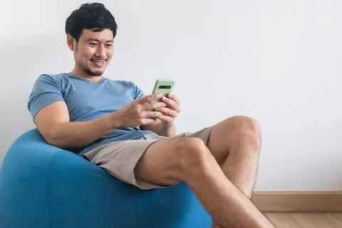 Happy man is using smartphone while sit and relax on the beans bag. Stock-Fotos