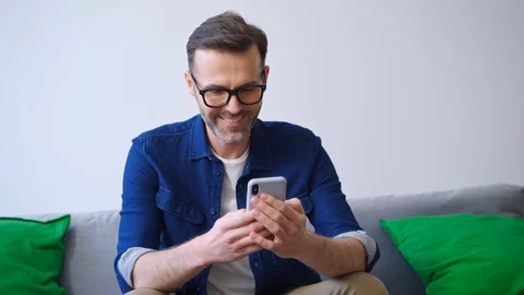 Happy man using smartphone withle sitting on sofa at home Video stock 127121550