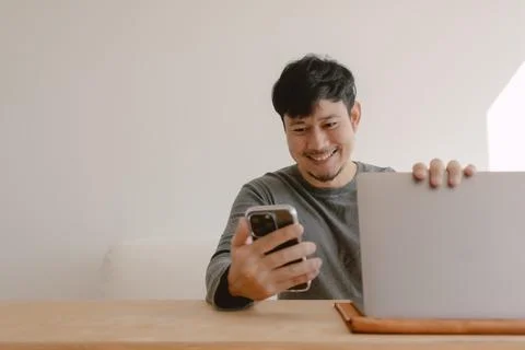 Happy man working on computer feeling happy with the app in mobile phone. Foto stock