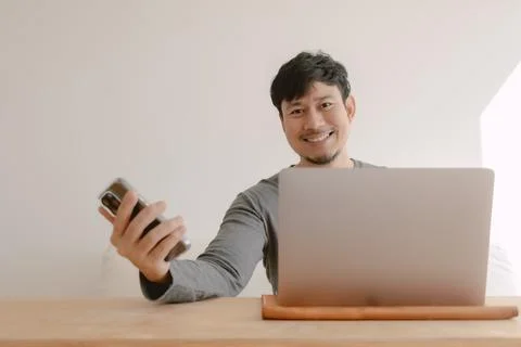 Happy man working on computer feeling happy with the app in mobile phone. Фото