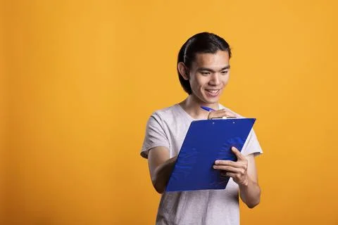 Happy man writing notes and checking tasks on clipboard in studio Foto stock