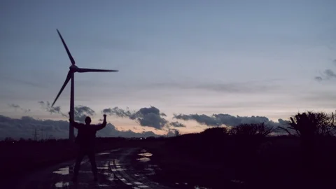 Happy mans silhouette jumping for joy, wind turbines at night Stock Footage 85749540