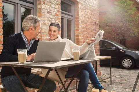 Happy mature couple reading newspaper with laptop in back yard Stock Photos