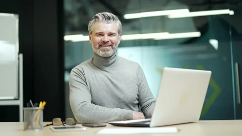 Happy mature gray-haired bearded businessman typing on laptop while sitting at  Stock Footage 232579188