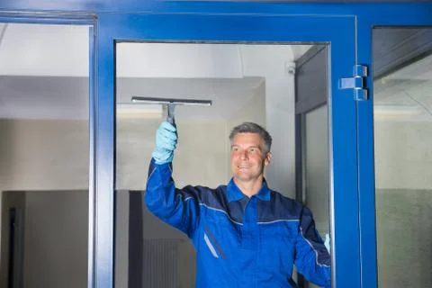 Happy mature male worker cleaning glass with squeegee Foto stock