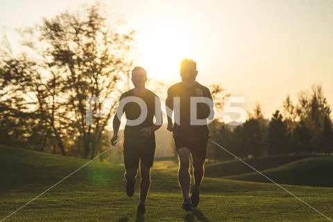 The happy men running on the park grass on the sunset background Stock Photos
