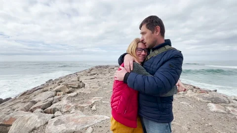 Happy middle-aged couple stands on a rocky breakwater by the Atlantic Ocean Vídeo Stock 319796351