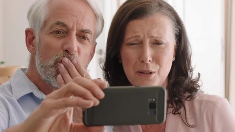 Happy middle aged couple using smartphone having video chat waving at Stock Footage