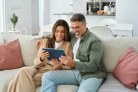 Happy middle aged couple using digital tablet relaxing on sofa at home. Stock-Fotos