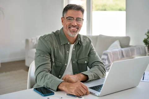 Happy middle aged man using laptop computer at home table. Portrait Stock Photos