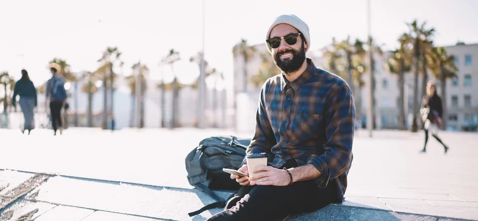 Happy Middle Eastern man in stylish hat and sunglasses using cellphone Stock Photos