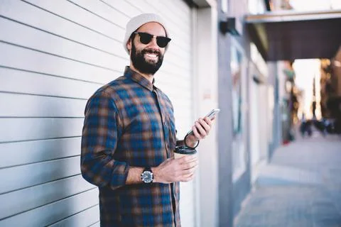 Happy Middle Eastern man in stylish hat and sunglasses using cellphone Stock Photos