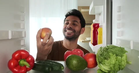 Happy Middle Eastern Man Takes an Apple from the Refrigerator and Takes a Bite Stock Footage 252667293