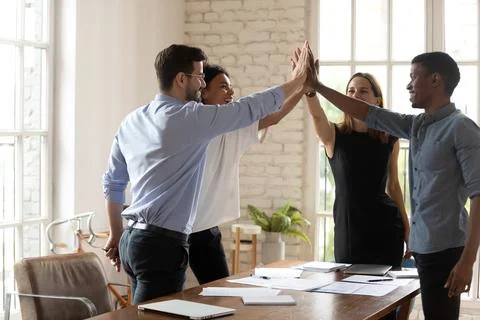 Happy mixed race colleagues giving high five in office. Stock Photos