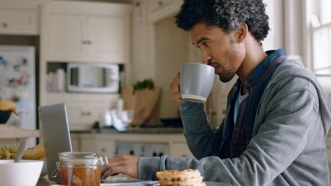 Happy mixed race man using laptop computer working at home in kitchen typing 動画素材 111720316