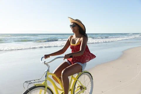 Happy mixed race woman on beach holiday riding bicycle on the sand by the sea Stock Photos