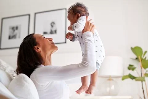 Happy mixed race young adult mother raising her three month old baby son in the Stock Photos