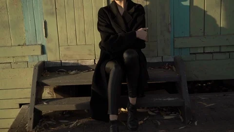 Happy model wrapped in stylish black coat relax on old wooden stairs on sunset Stock Footage 124732133
