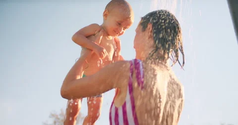 Happy mother and baby boy take fun together in sunlights shower outdoor. Young Stock Footage