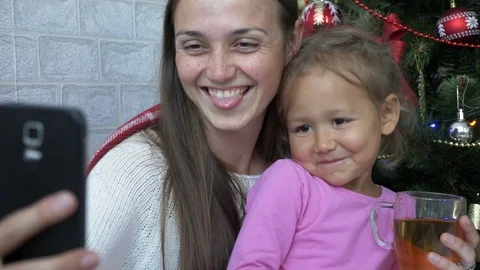Happy mother and daughter plaing the ape and doing selfie next to Christmas tree Stock Footage